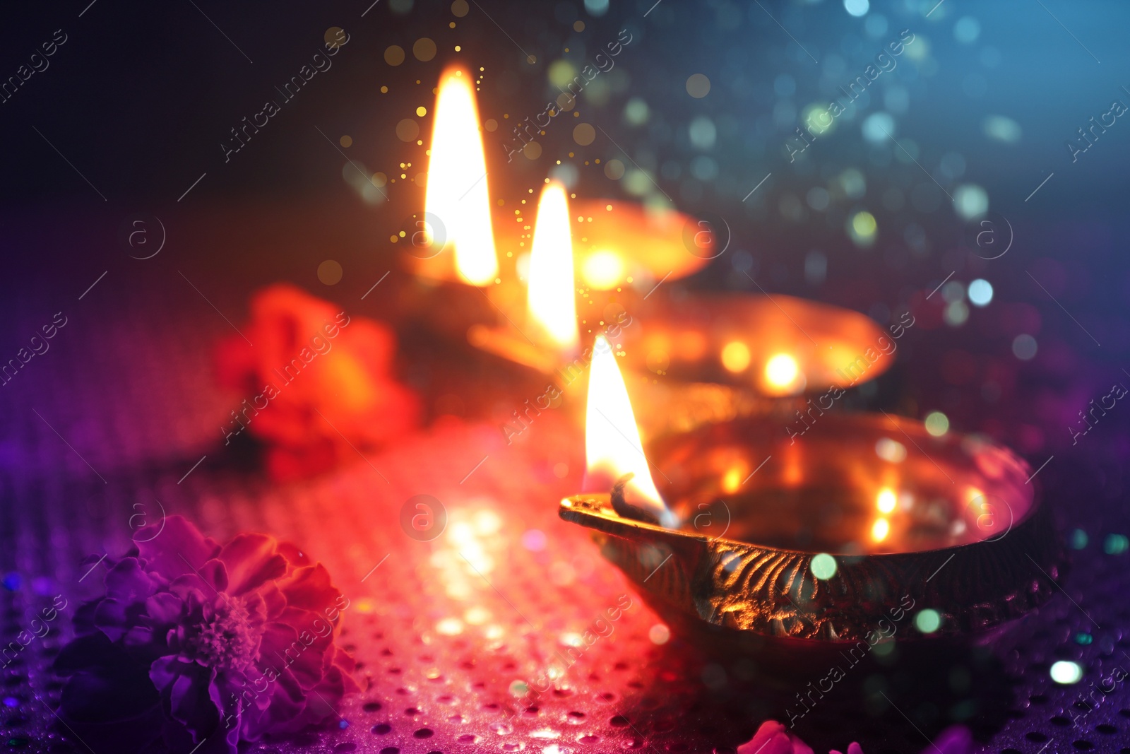 Image of Happy Diwali celebration. Diya lamps burning and beautiful flowers on dark background, closeup. Bokeh effect