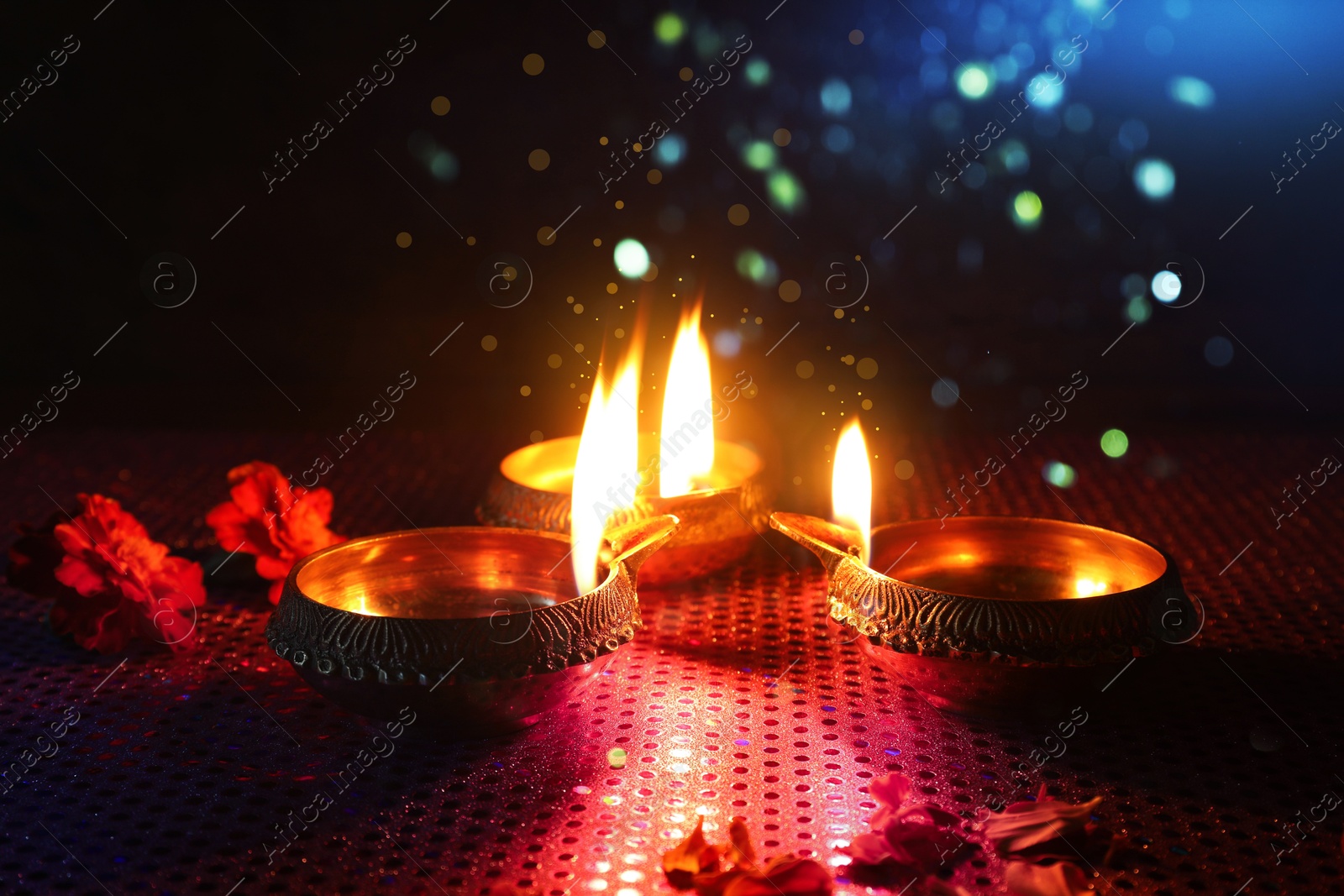 Image of Happy Diwali celebration. Diya lamps burning and beautiful flowers on dark background, closeup. Bokeh effect