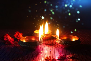 Image of Happy Diwali celebration. Diya lamps burning and beautiful flowers on dark background, closeup. Bokeh effect