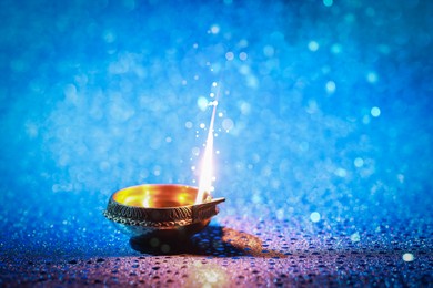 Happy Diwali celebration. Diya lamp burning on blue background. Space for text. Bokeh effect