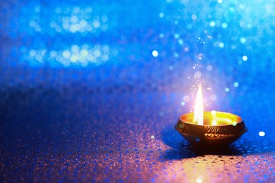 Happy Diwali celebration. Diya lamp burning on blue background. Space for text. Bokeh effect