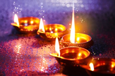 Happy Diwali celebration. Diya lamps burning on color background, closeup. Bokeh effect