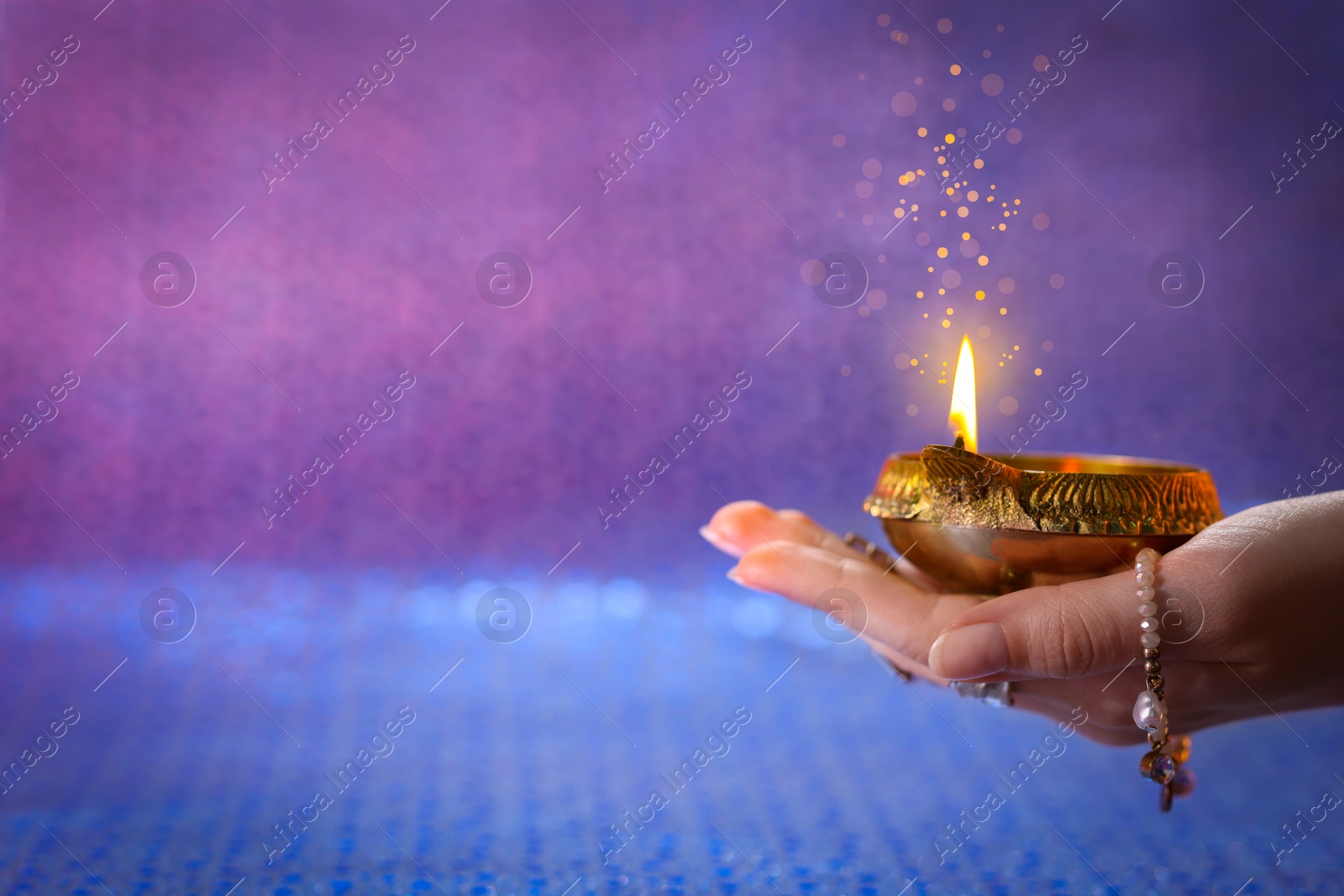 Image of Happy Diwali celebration. Woman holding lit diya lamp on color background, closeup. Space for text. Bokeh effect