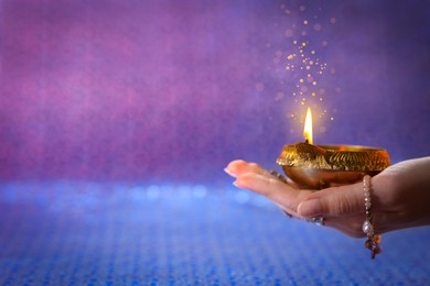 Image of Happy Diwali celebration. Woman holding lit diya lamp on color background, closeup. Space for text. Bokeh effect