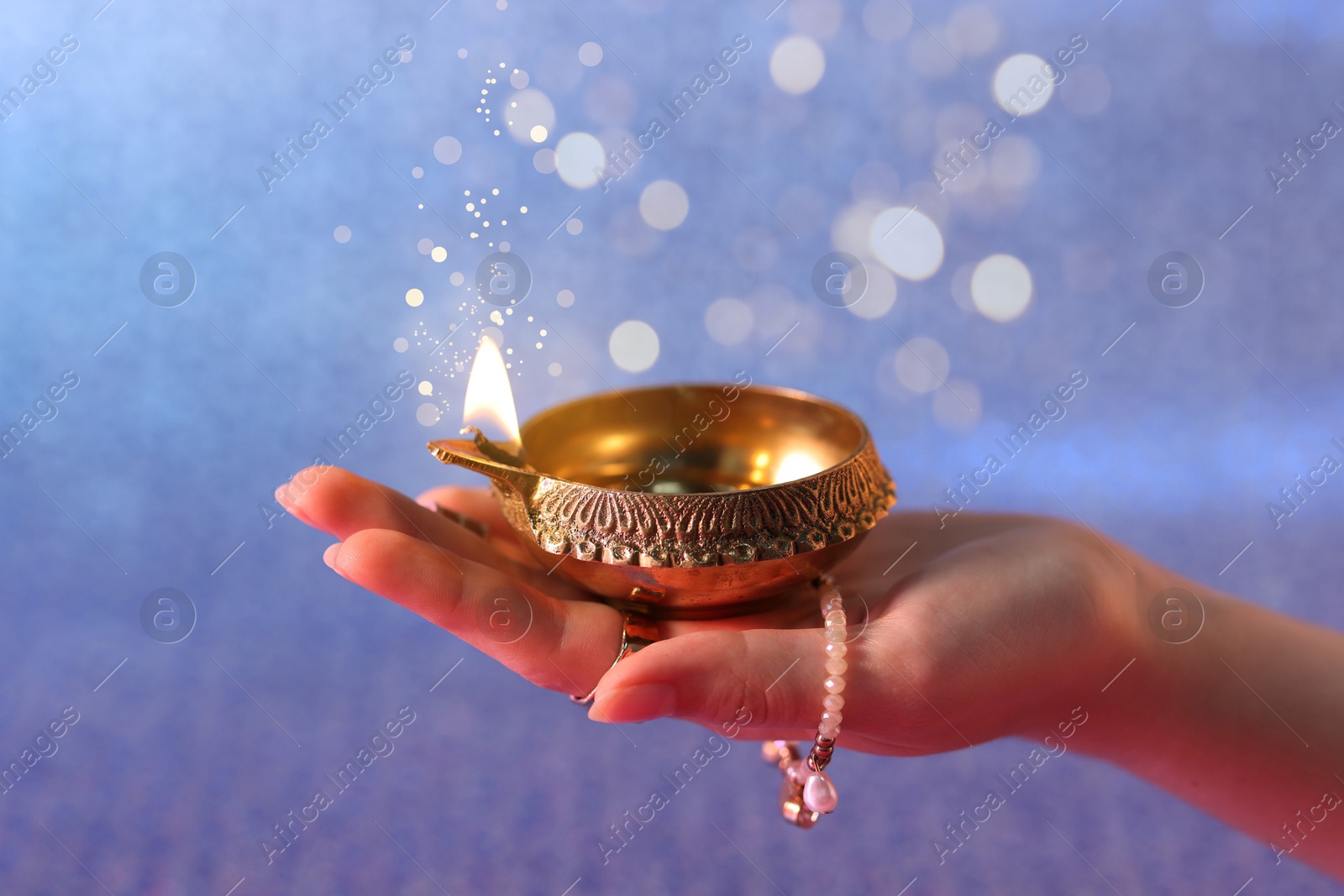 Image of Happy Diwali celebration. Woman holding lit diya lamp on color background, closeup. Bokeh effect