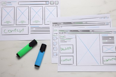 Photo of Developing UI design. Sketches of website wireframes and felt pens on white marble table, top view