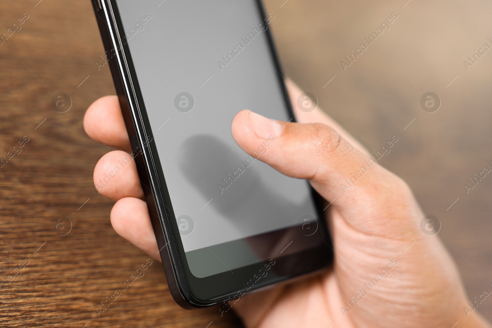 Photo of Man unlocking smartphone with fingerprint scanner at wooden table, closeup