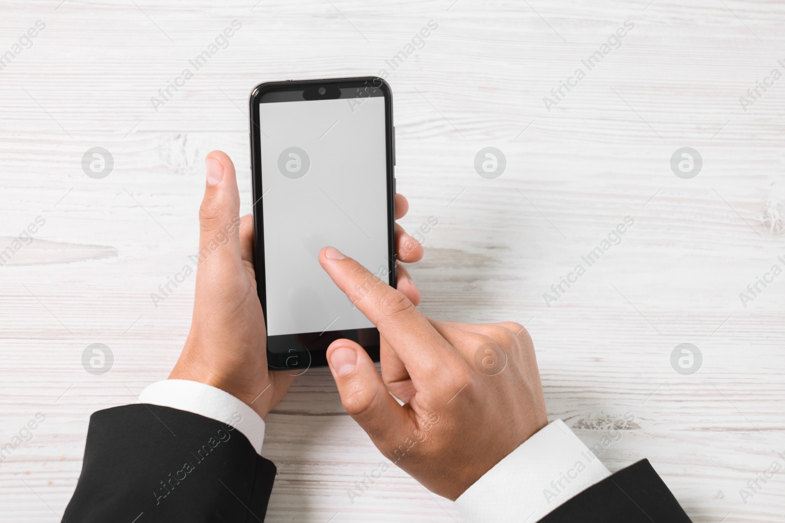 Photo of Man unlocking smartphone with fingerprint scanner at light wooden table, top view