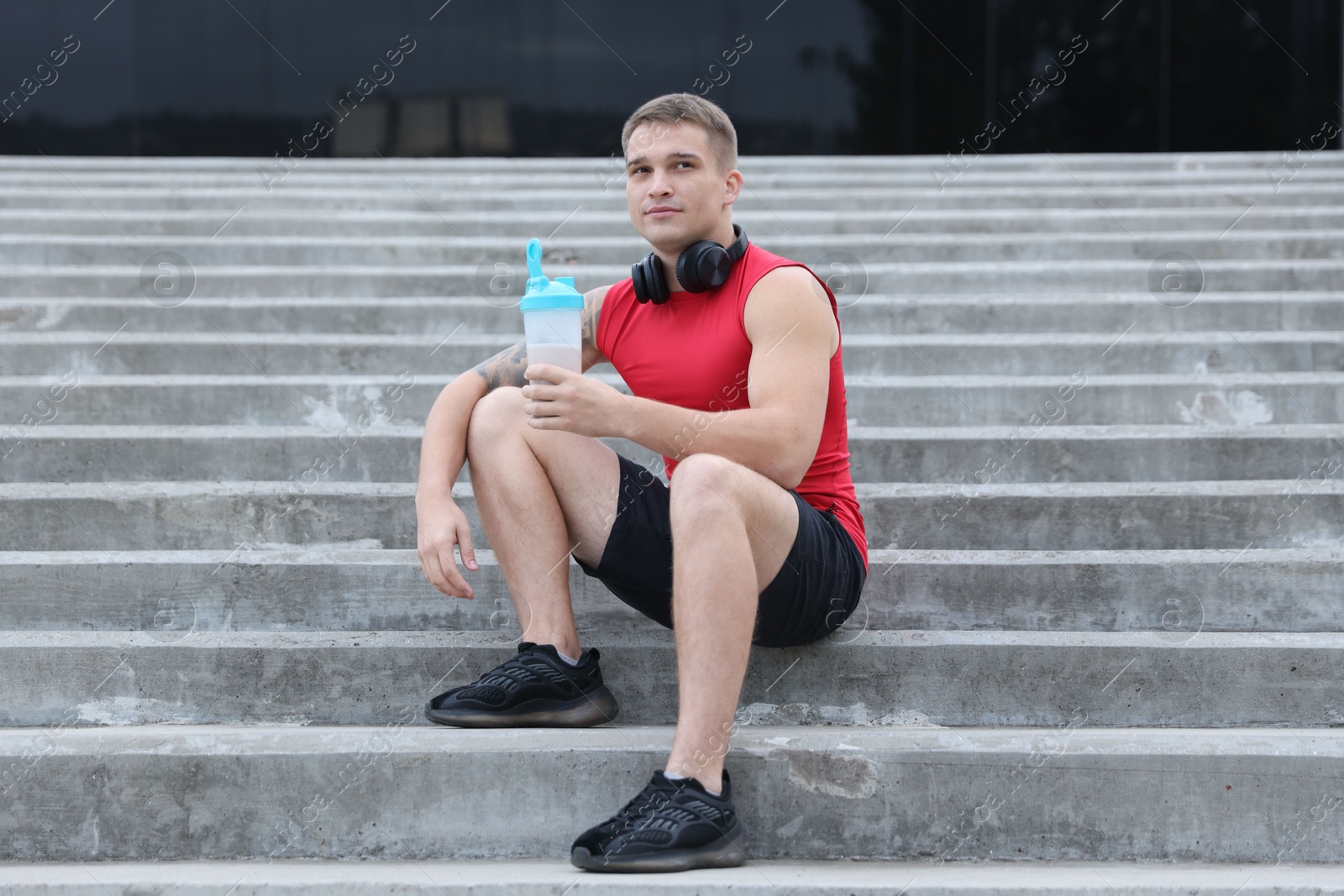 Photo of Athletic man with shaker of protein drink sitting on stairs outdoors