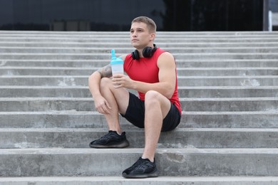 Photo of Athletic man with shaker of protein drink sitting on stairs outdoors