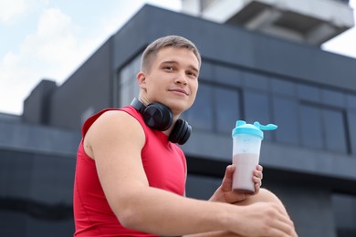 Photo of Athletic man with shaker of protein drink outdoors, low angle view