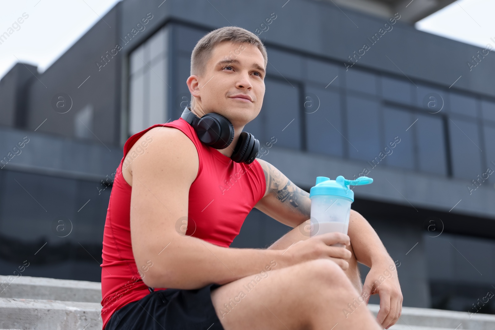 Photo of Athletic man with shaker of protein drink outdoors, low angle view