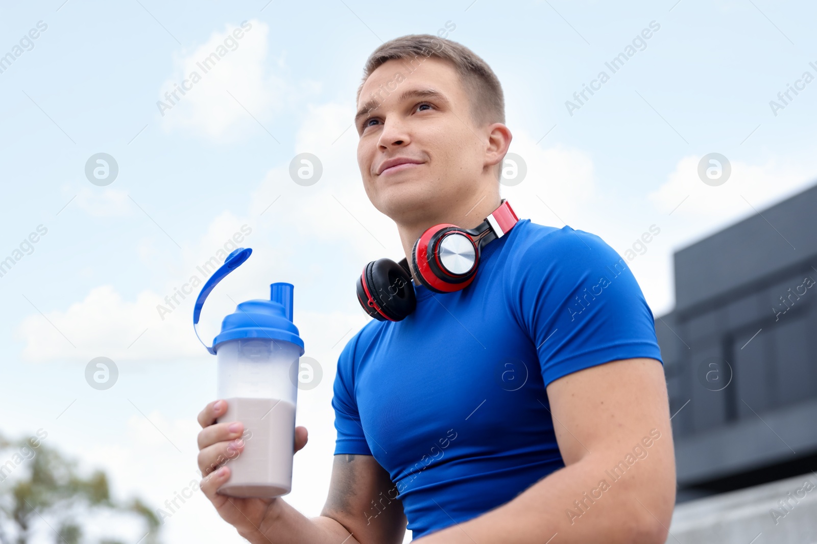 Photo of Athletic man with shaker of protein drink outdoors, low angle view