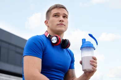 Photo of Athletic man with shaker of protein drink outdoors, low angle view