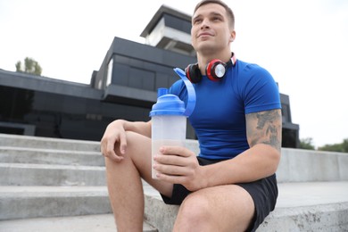 Photo of Athletic man with shaker of protein drink outdoors, low angle view