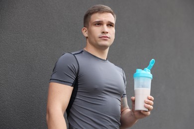 Athletic man with shaker of protein drink near grey wall