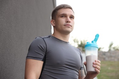 Photo of Athletic man with shaker of protein drink near grey wall outdoors