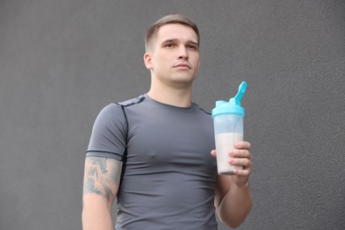 Photo of Athletic man with shaker of protein drink near grey wall