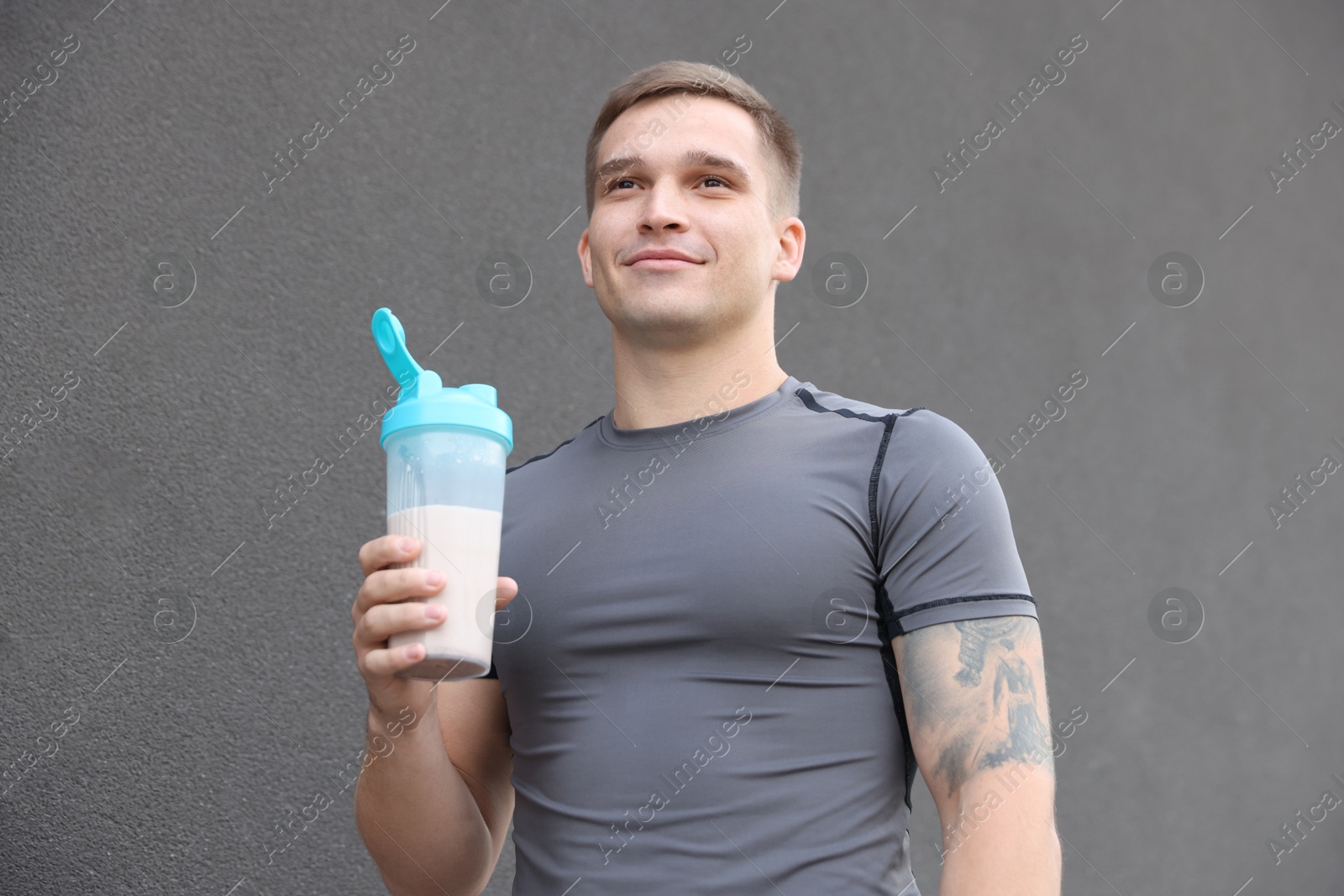 Photo of Athletic man with shaker of protein drink near grey wall