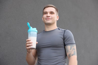 Photo of Athletic man with shaker of protein drink near grey wall