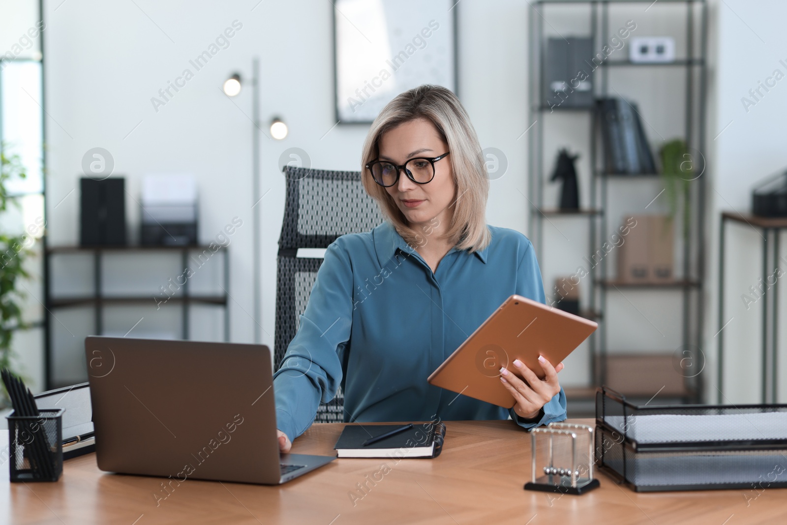 Photo of Businesswoman with tablet working on laptop at table in office