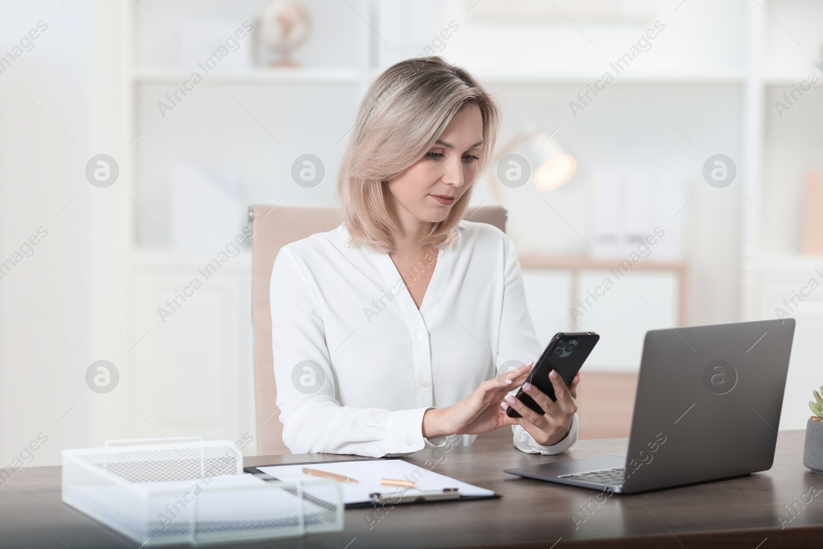 Photo of Businesswoman using smartphone at table in office