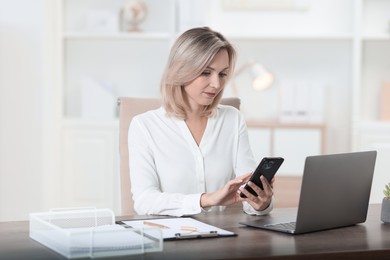 Photo of Businesswoman using smartphone at table in office