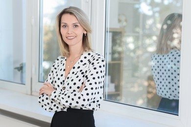 Photo of Happy businesswoman with crossed arms near window in office