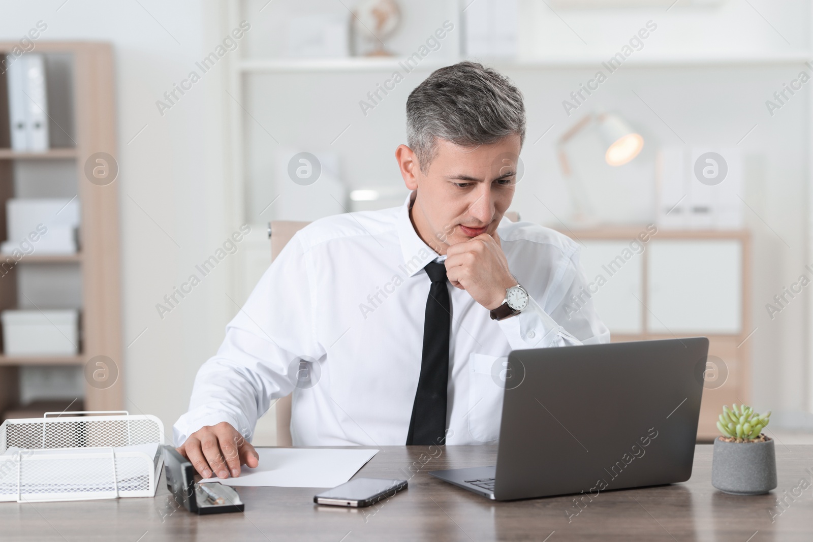 Photo of Businessman working with laptop at table in office