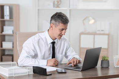 Photo of Businessman working with laptop at table in office