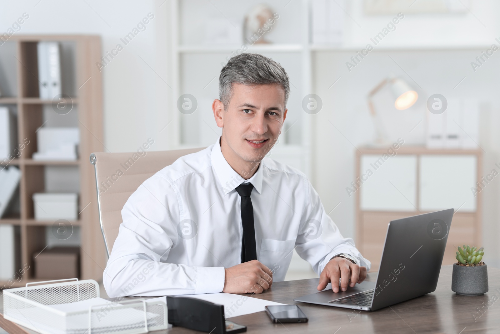 Photo of Businessman working with laptop at table in office