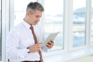 Photo of Businessman using tablet near window in office, space for text