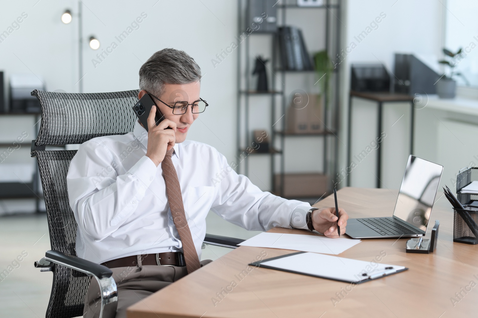 Photo of Businessman talking on smartphone at table in office