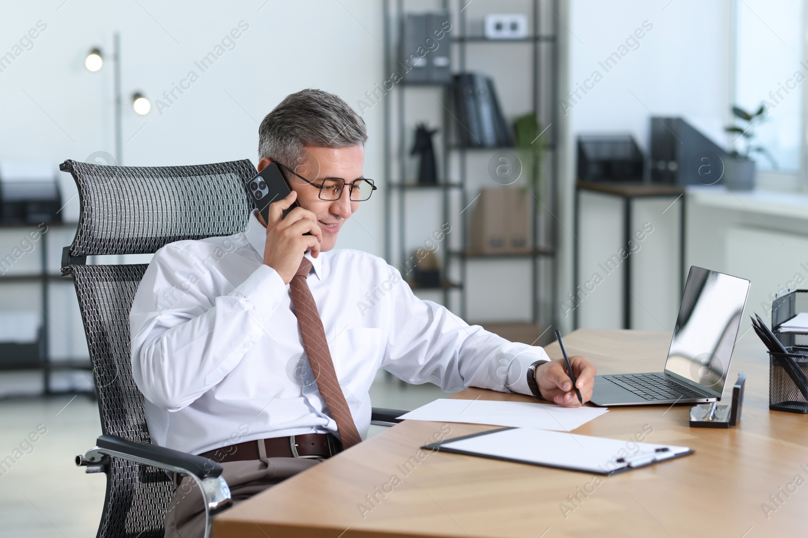 Photo of Businessman talking on smartphone at table in office