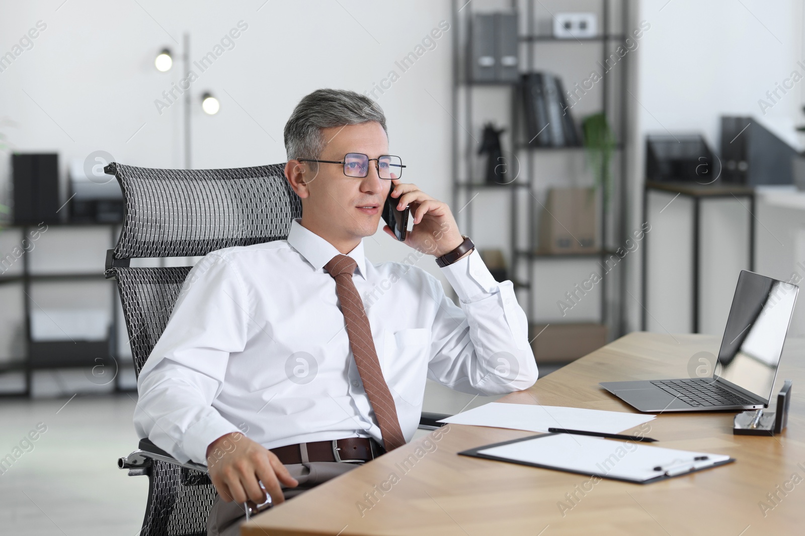 Photo of Businessman talking on smartphone at table in office