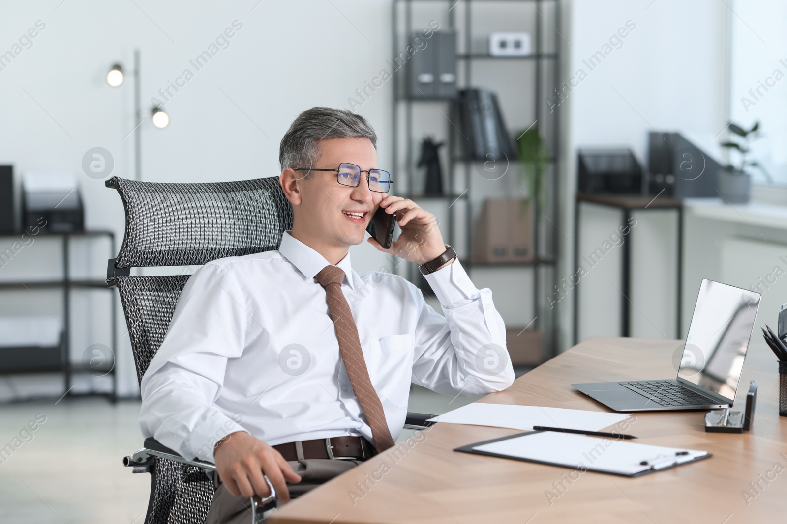 Photo of Businessman talking on smartphone at table in office