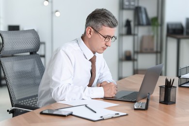 Photo of Businessman working on laptop at table in office