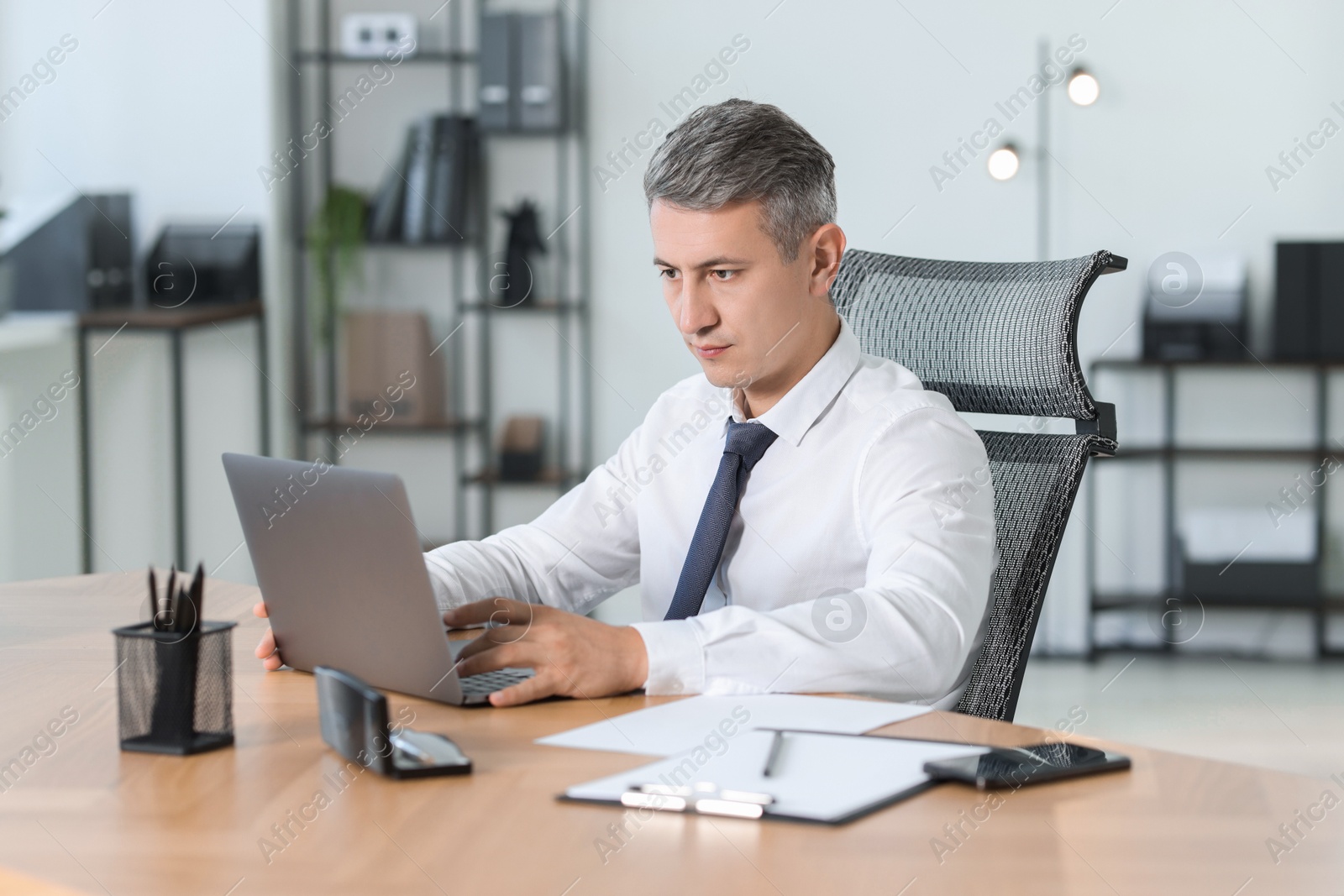 Photo of Businessman working on laptop at table in office