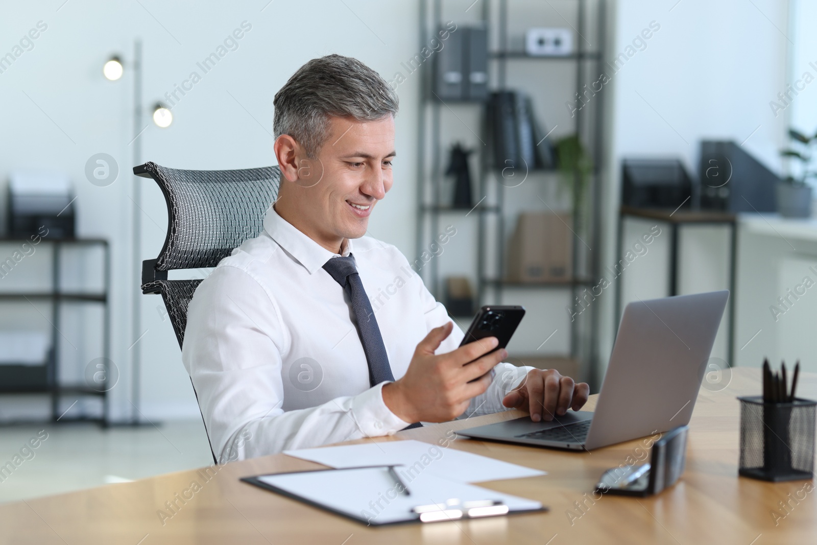 Photo of Businessman with smartphone working on laptop at table in office