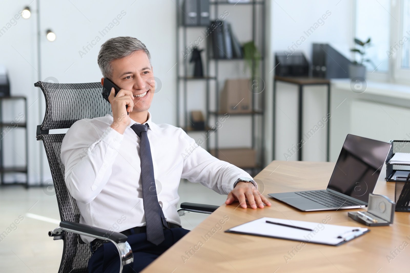 Photo of Businessman talking on smartphone at table in office