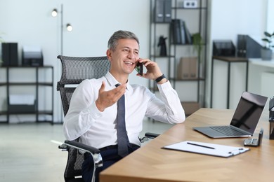 Photo of Businessman talking on smartphone at table in office