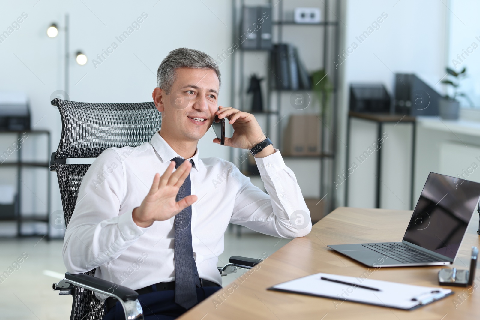 Photo of Businessman talking on smartphone at table in office