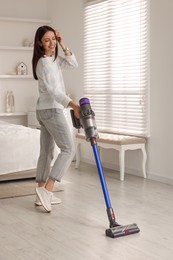 Photo of Smiling young woman cleaning floor with cordless vacuum cleaner in bedroom