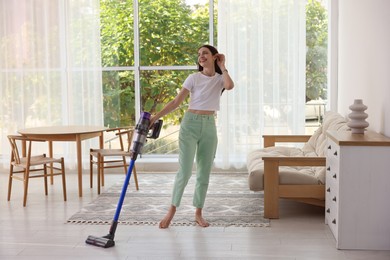 Photo of Smiling young woman cleaning floor with cordless vacuum cleaner at home