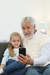 Grandpa and his granddaughter watching something on smartphone at home