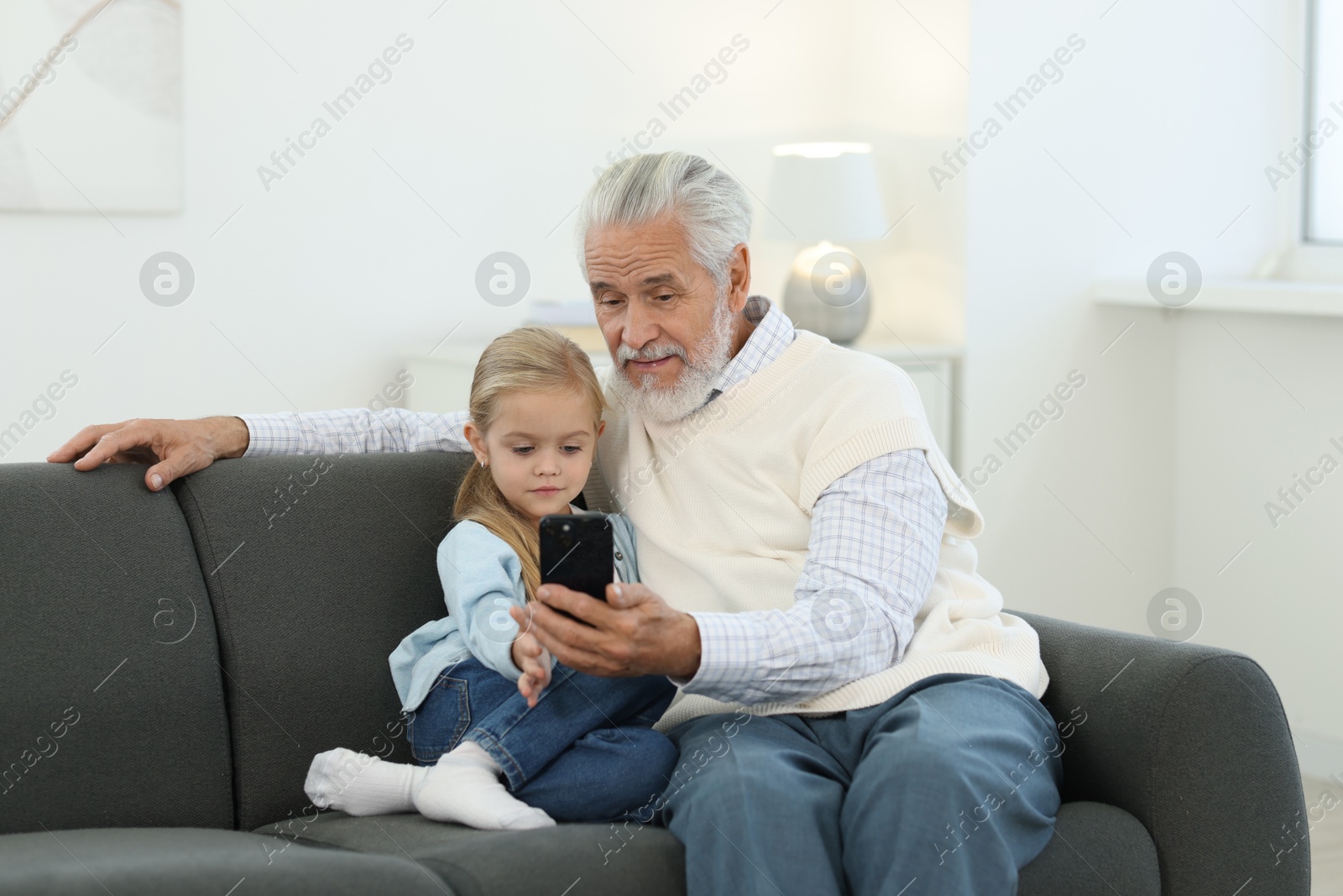 Photo of Grandpa and his granddaughter watching something on smartphone at home