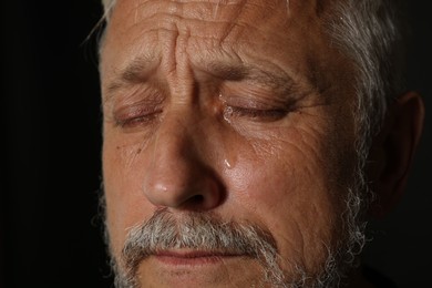 Photo of Sad senior man crying on black background, closeup