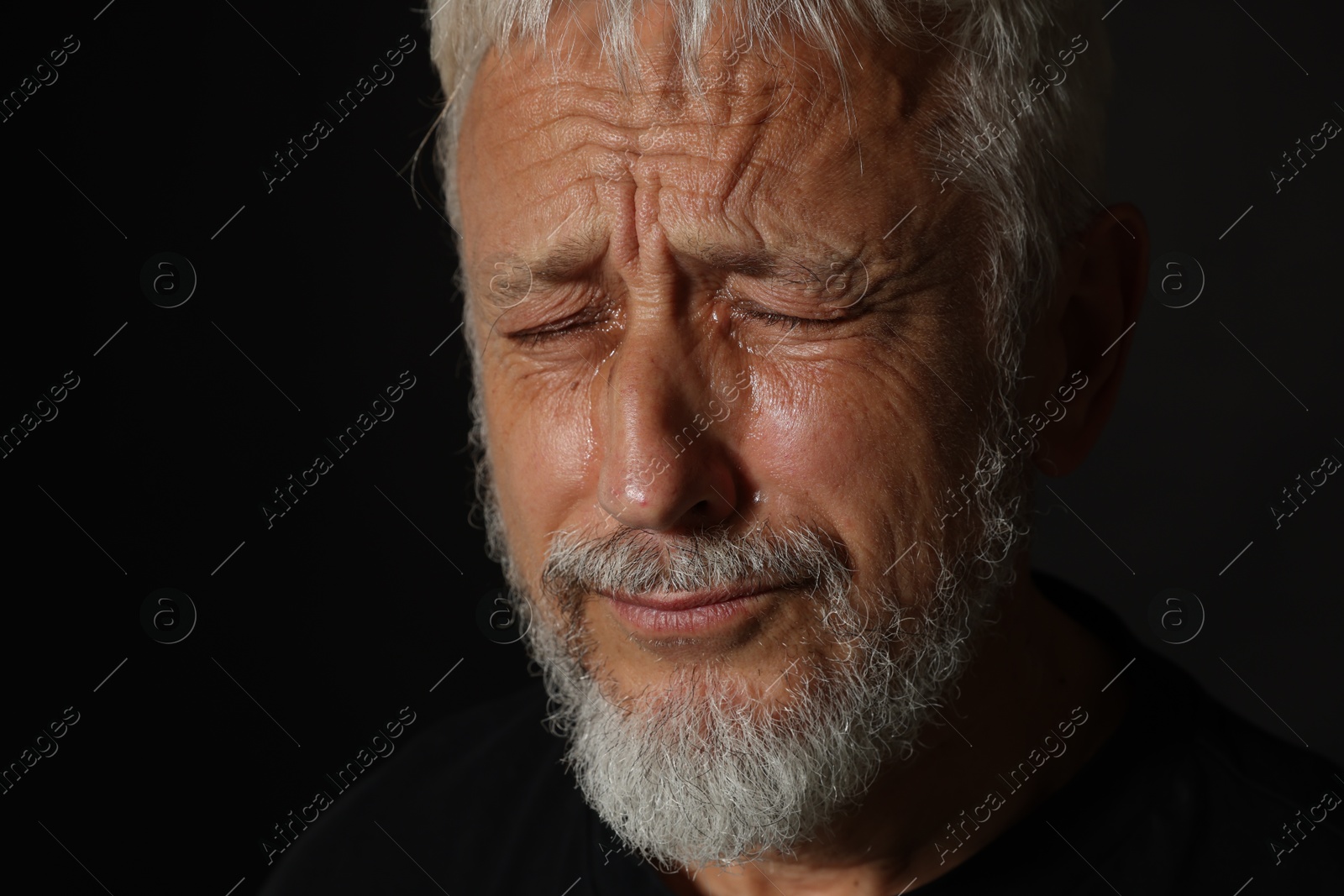 Photo of Sad senior man crying on black background, closeup