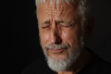 Photo of Sad senior man crying on black background, closeup