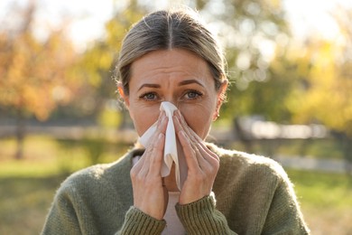 Woman with tissue blowing runny nose in park